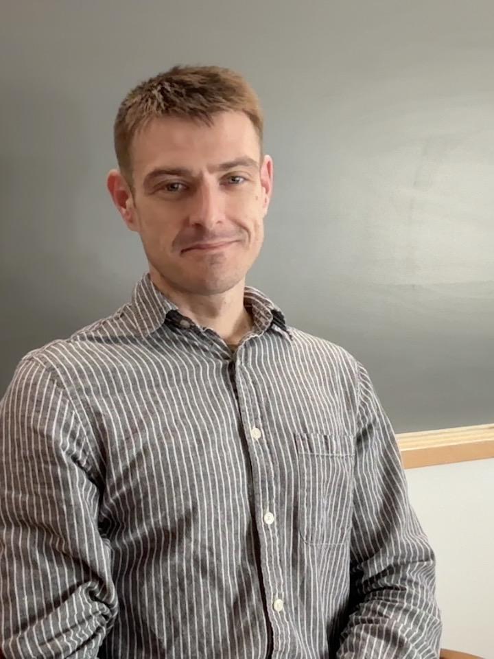 Postdoc, Zach Maschman, sitting in front of a blackboard in a classroom